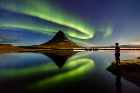 A man watching a spectacular show of aurora borealis over a body of water