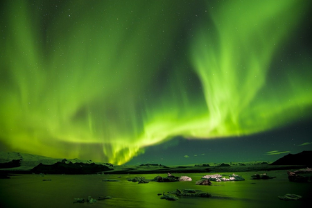 A green-hued display of the Northern Lights over a body of water in Iceland